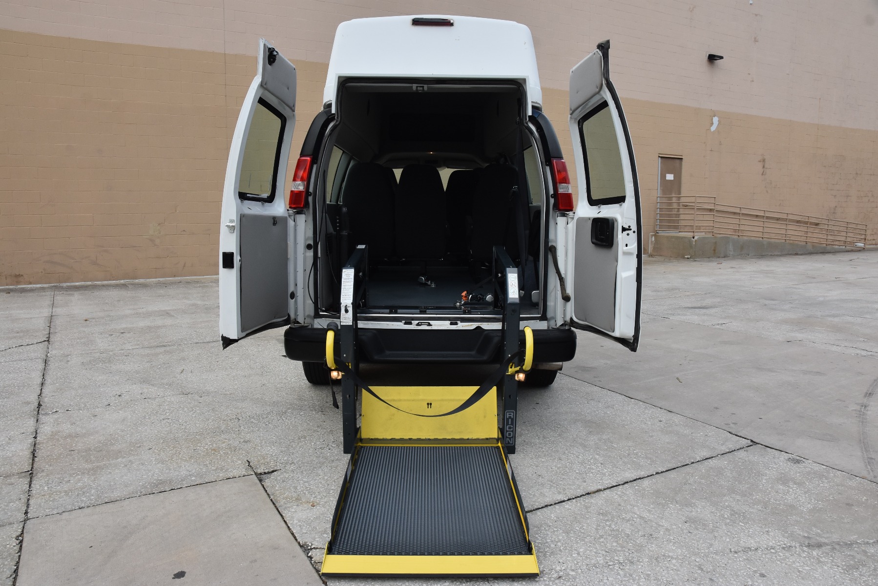 White Chevrolet Express Full Size Wheelchair Van with lift deployed from open rear barn doors.