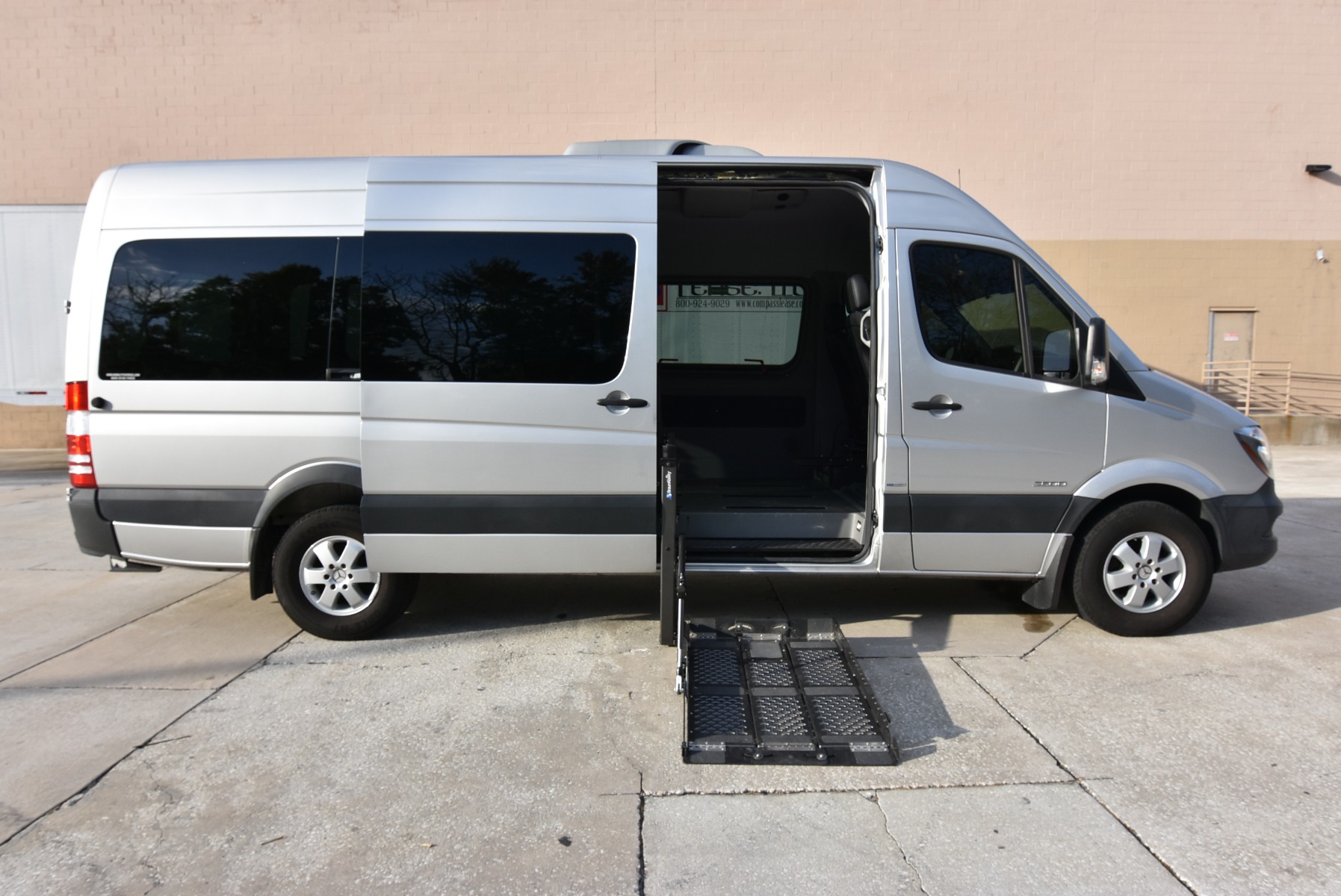 Silver Mercedes Sprinter full size wheelchair van with lift deployed from open passenger side sliding door.