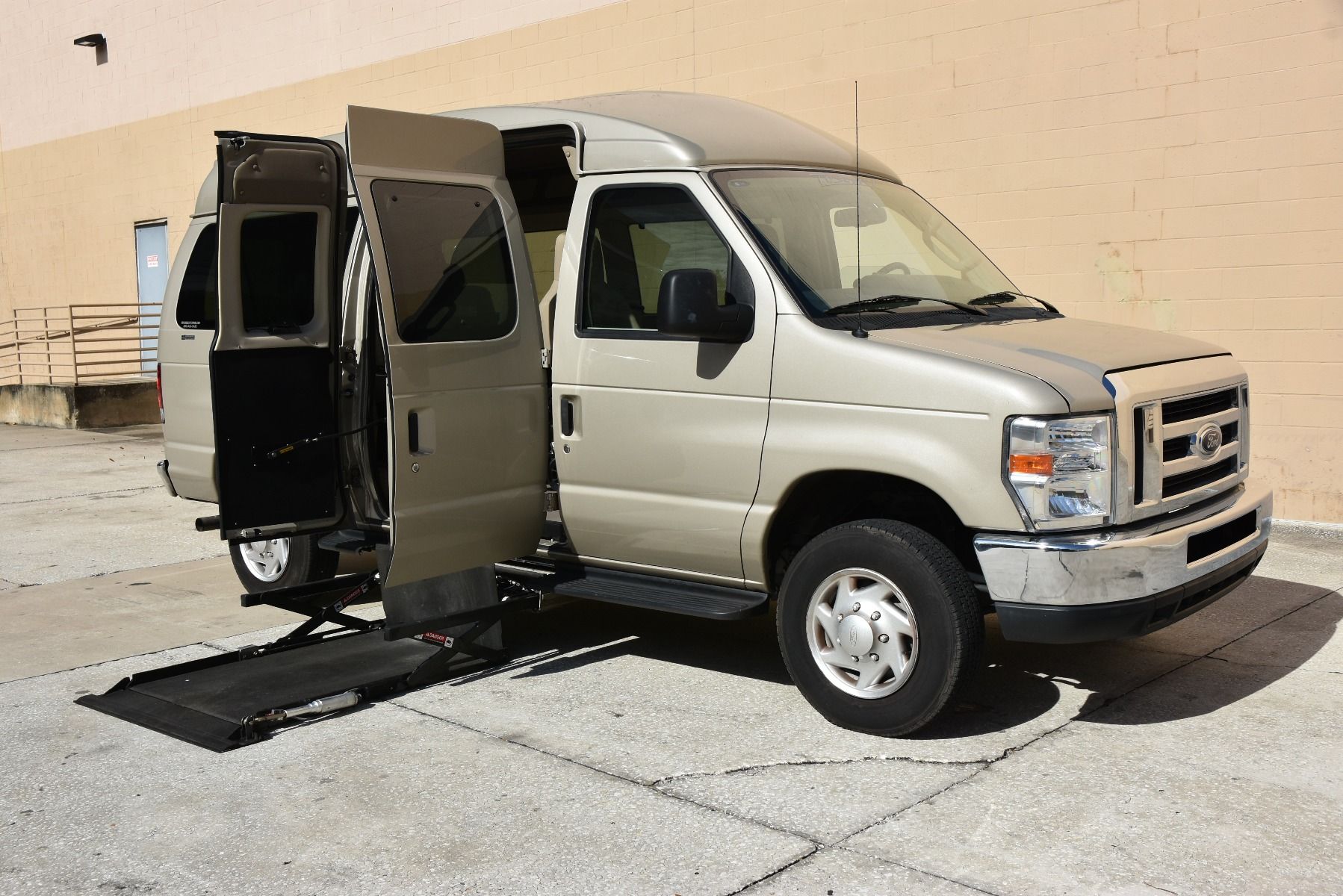 Passenger Side of a Gold 2013 Ford E-350 Full Size Wheelchair Van with Lift Deployed from the middle doors.